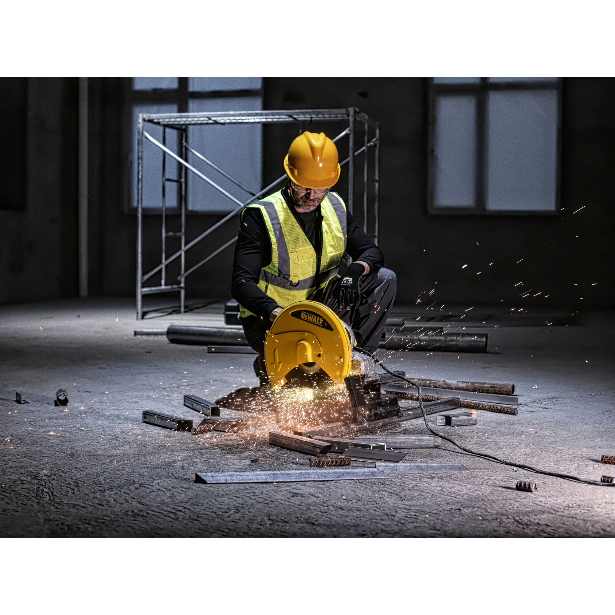 A construction worker wearing a safety vest and helmet is using a DEWALT D28730 cut-off saw to cut metal rods. Sparks are flying from the saw while working indoors at a construction site.