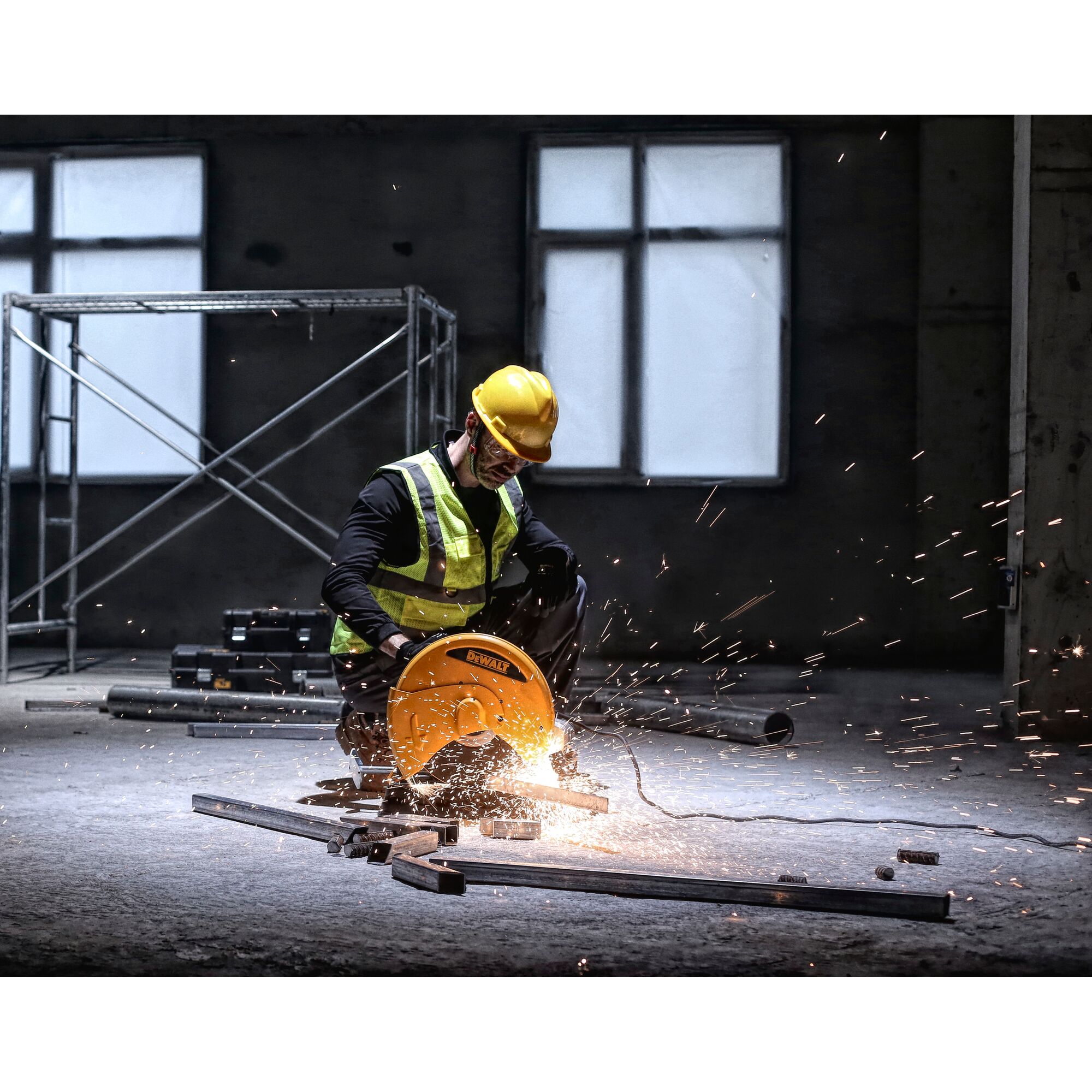 A worker wearing a yellow safety helmet and high-visibility vest is using a DEWALT metal cutting saw to cut steel bars indoors. Sparks are flying from the saw as it operates.