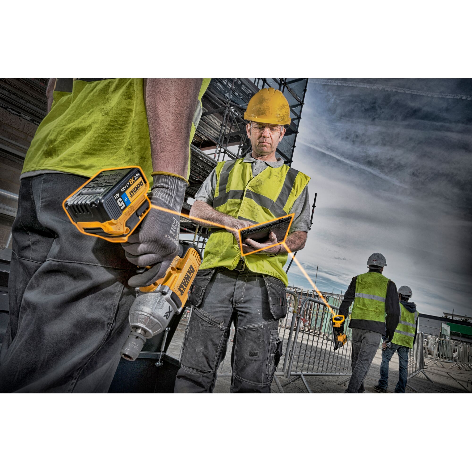 Construction workers wearing safety vests and helmets are on an outdoor building site. One worker holds a DEWALT power tool with a DCB184 battery, while another checks a tablet. In the background, two more workers walk near scaffolding.