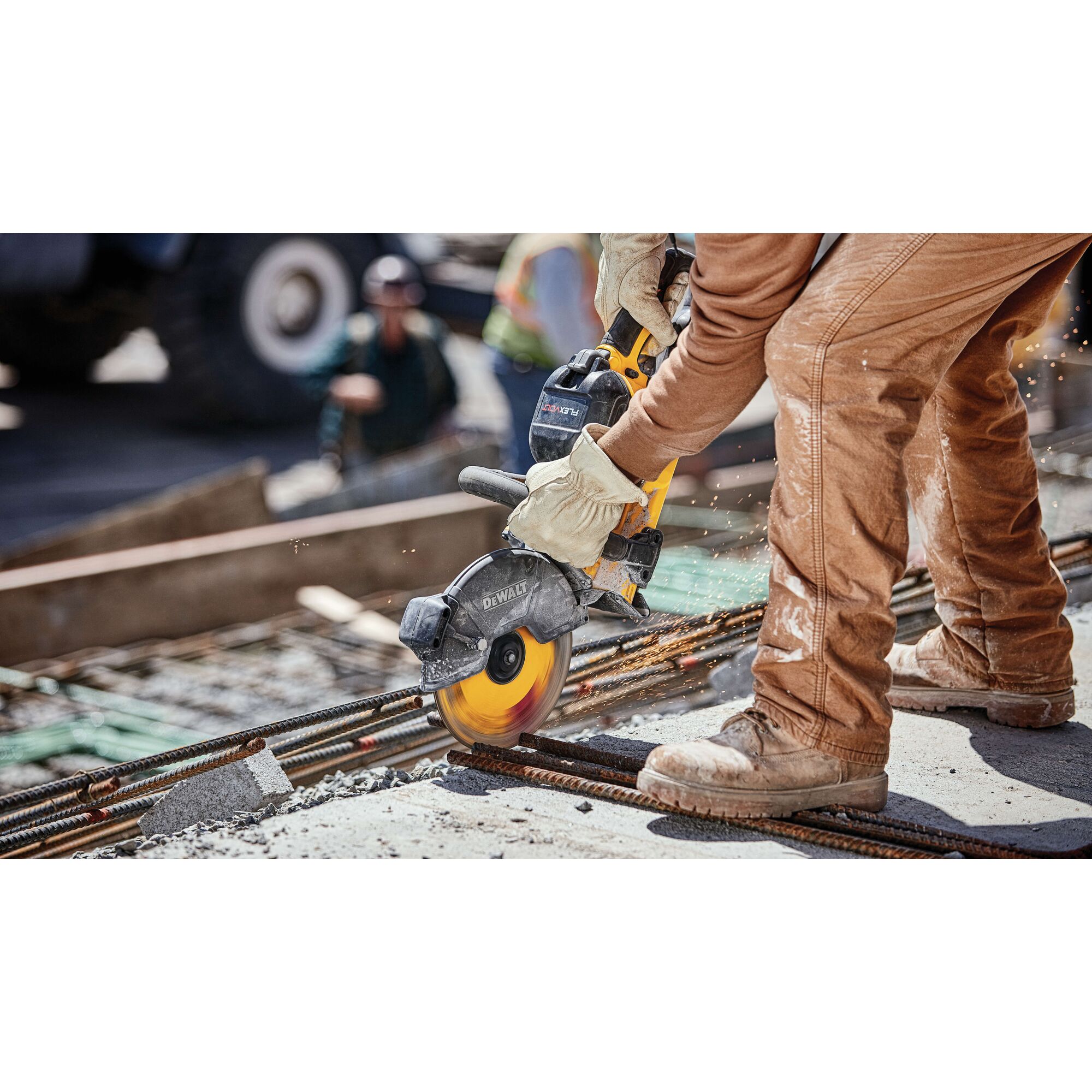 A worker wearing protective gloves and brown work clothes is using a DEWALT power saw to cut metal rebar on a construction site.