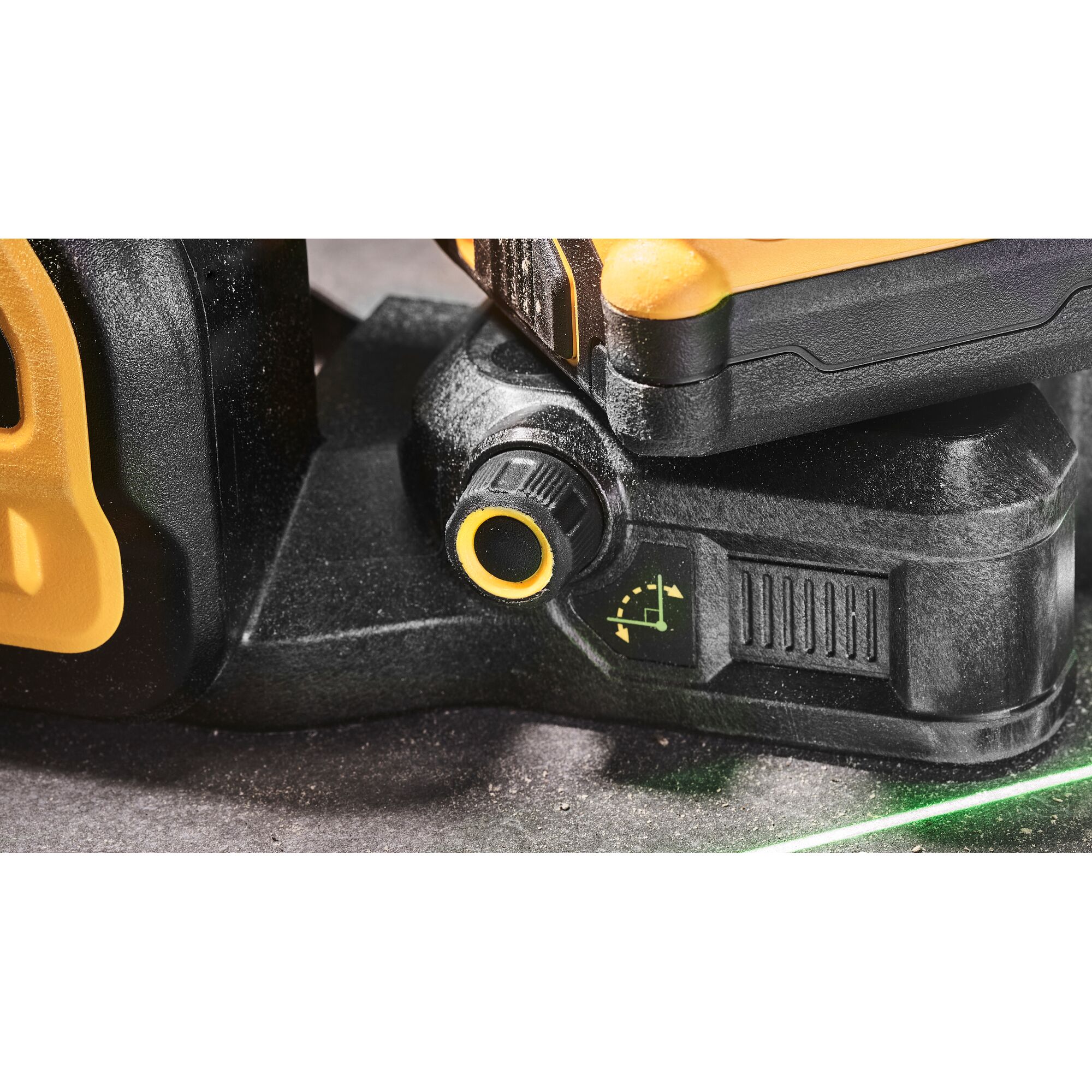 Close-up view of a DEWALT laser level adjustment knob and base, showing a yellow and black design with a control dial and an angle adjustment indicator. A green laser line is visible on the surface below.