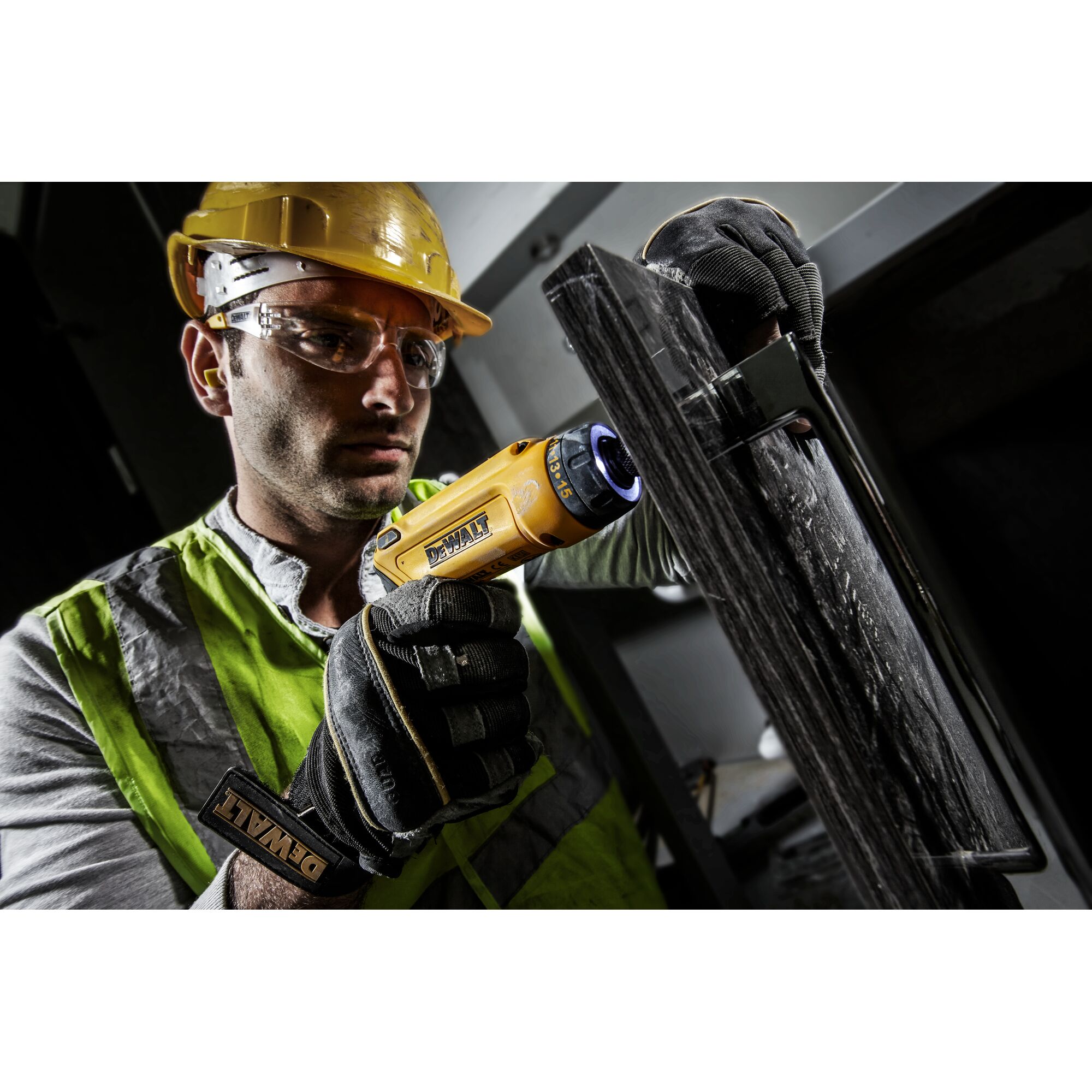 Person using a DEWALT electric screwdriver on a dark surface, wearing gloves and safety gear.