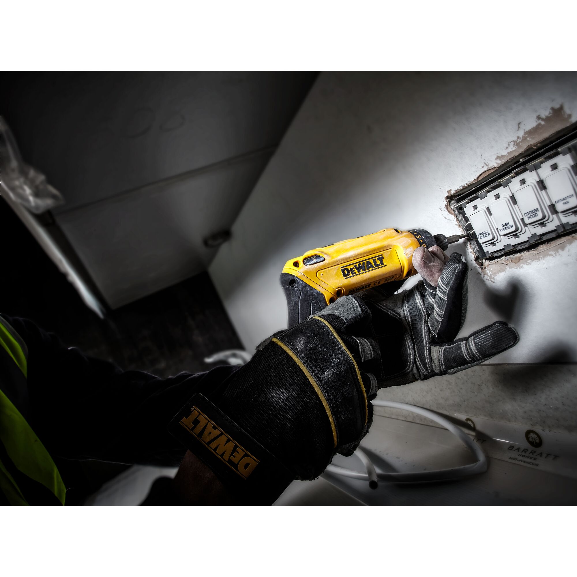 Gloved hand uses DEWALT DCF680G2 screwdriver near an electrical outlet on a wall.