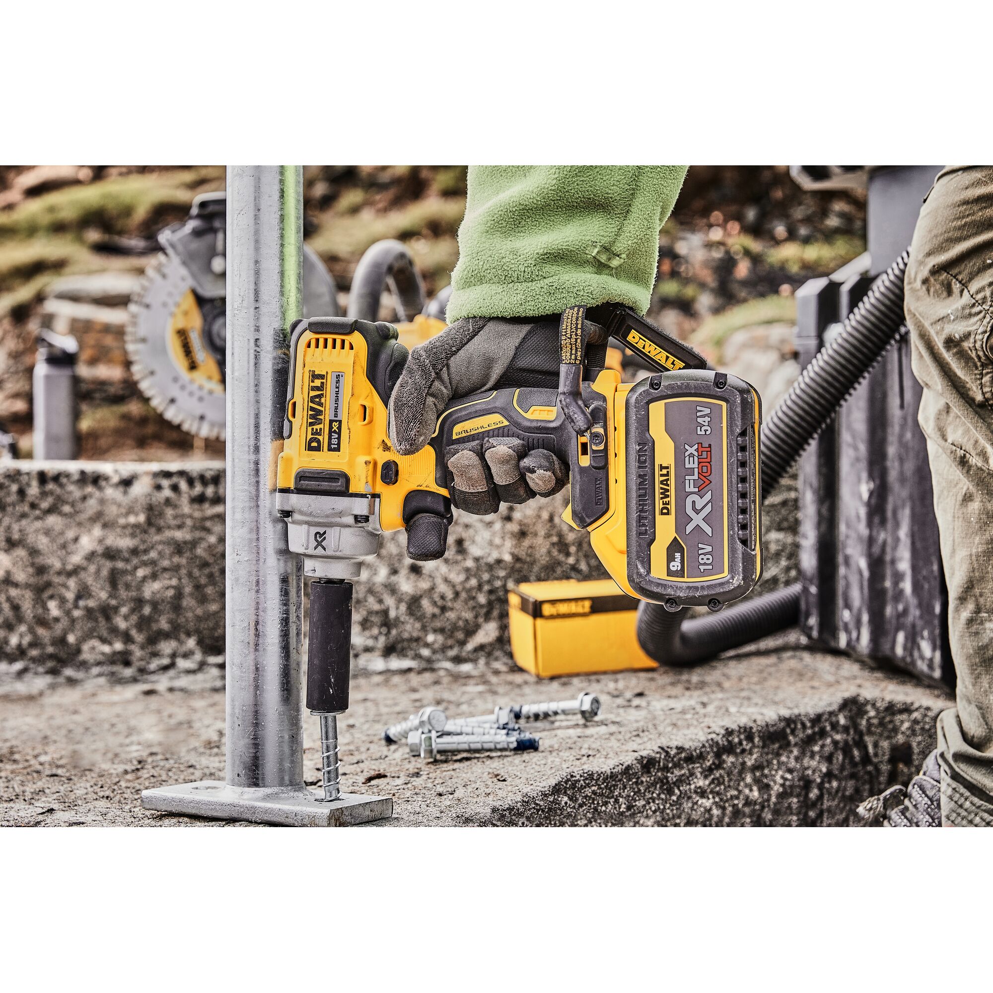 A DEWALT cordless impact wrench (DCF894P2) being used to fasten a bolt on a metal base outdoors. The tool is held by a gloved hand, with several bolts and a DEWALT tool box visible in the background.