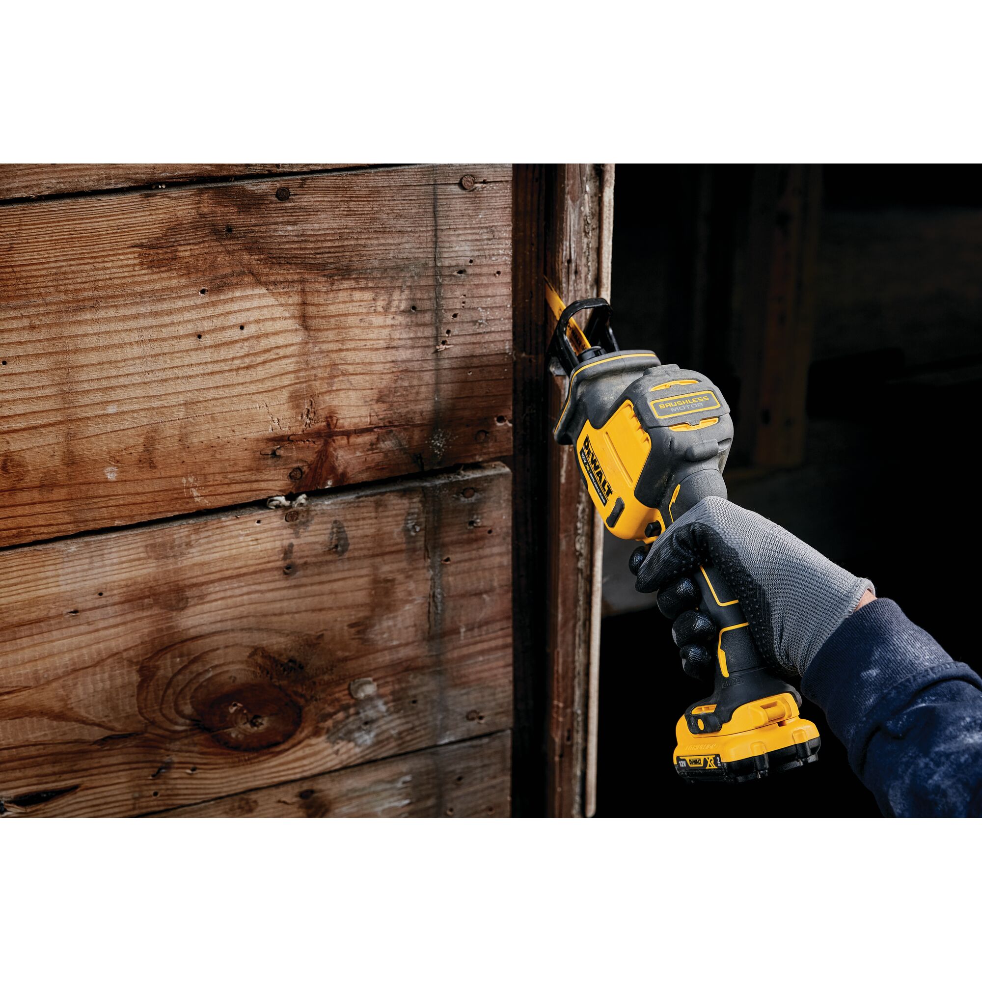Person uses a DEWALT reciprocating saw to cut wood near a wall. Gloved hand holds the yellow and black tool.