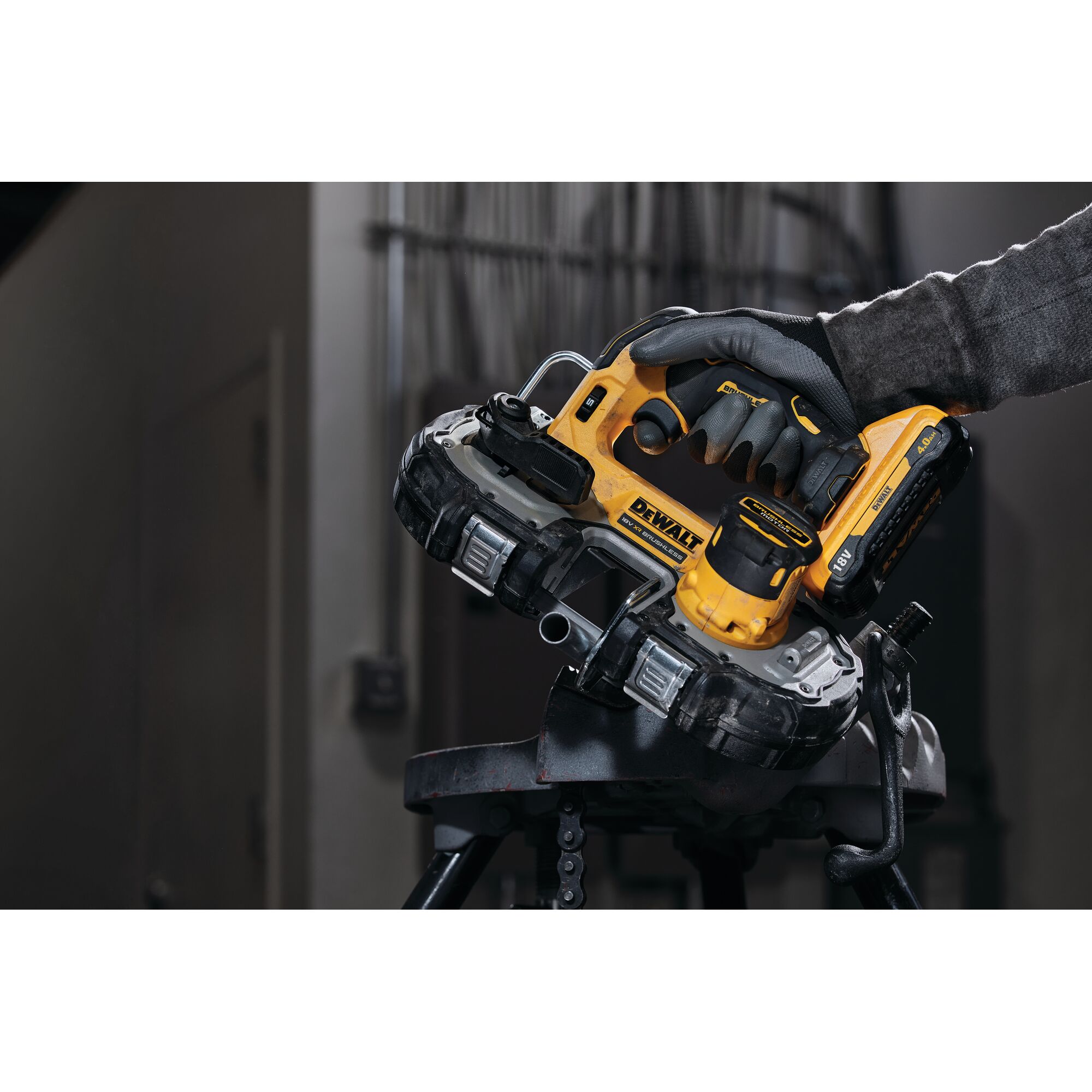 A close-up of a person using a yellow and black DEWALT cordless band saw (model DCS377NT) to cut through a metal pipe in an indoor workshop setting.