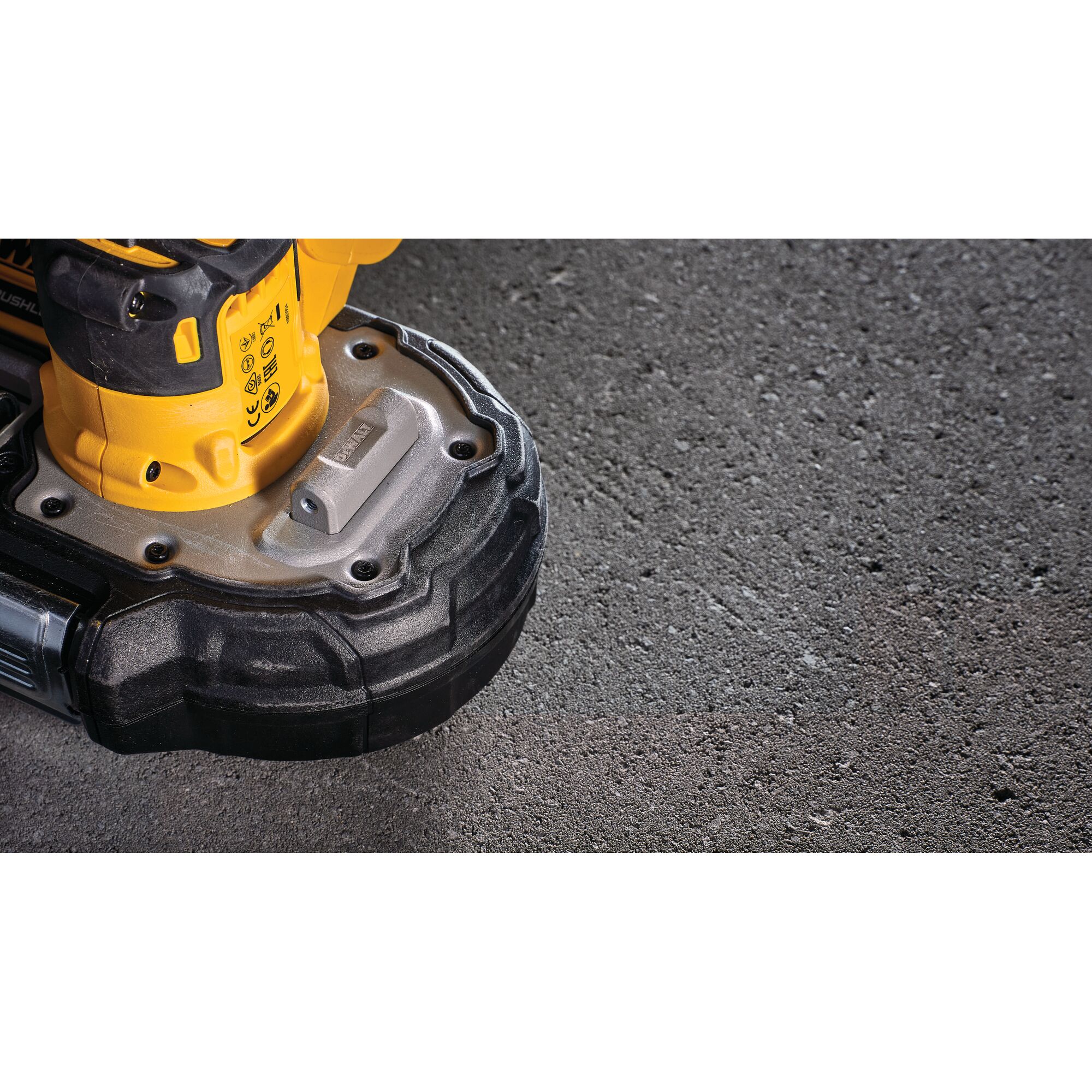 Close-up view of the base of a yellow and black DEWALT power tool resting on a textured concrete surface.