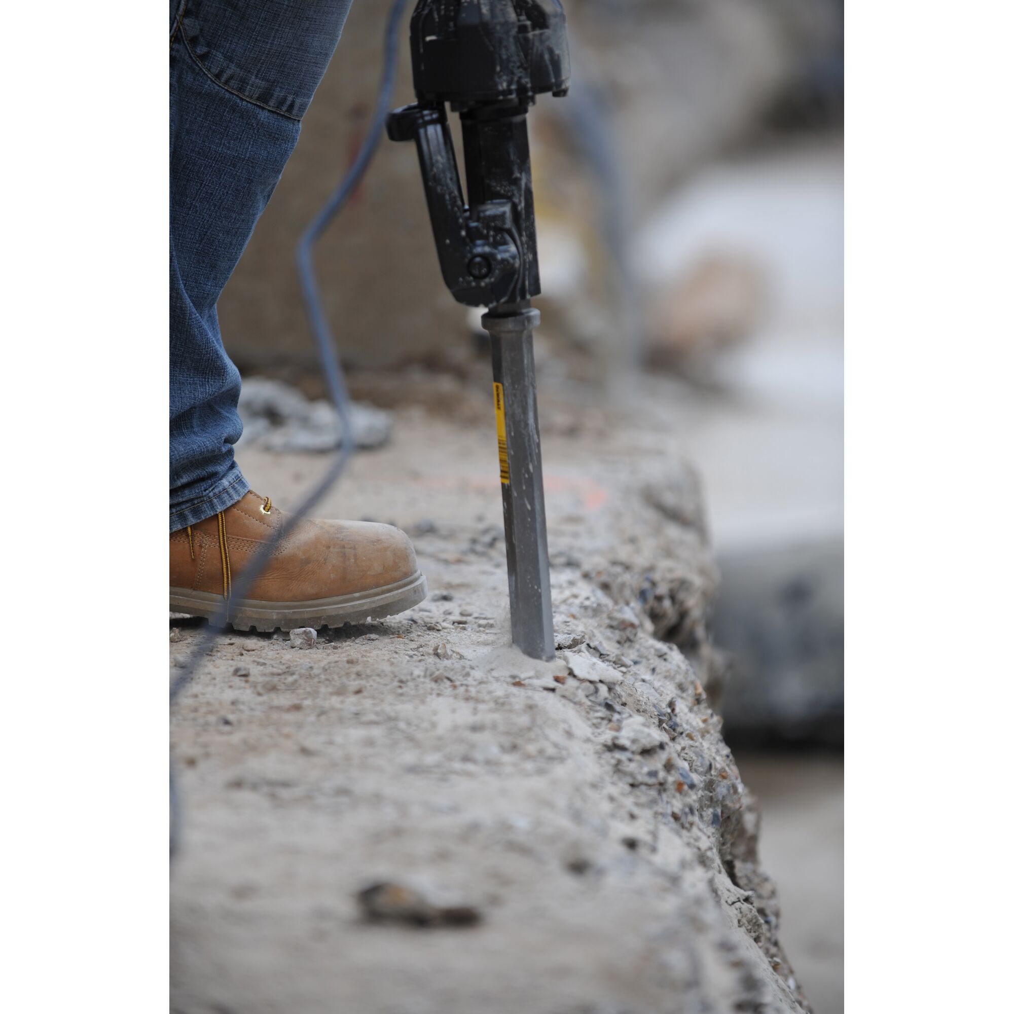 Worker uses a rotary hammer with a chisel bit drilling into concrete slab on a construction site.