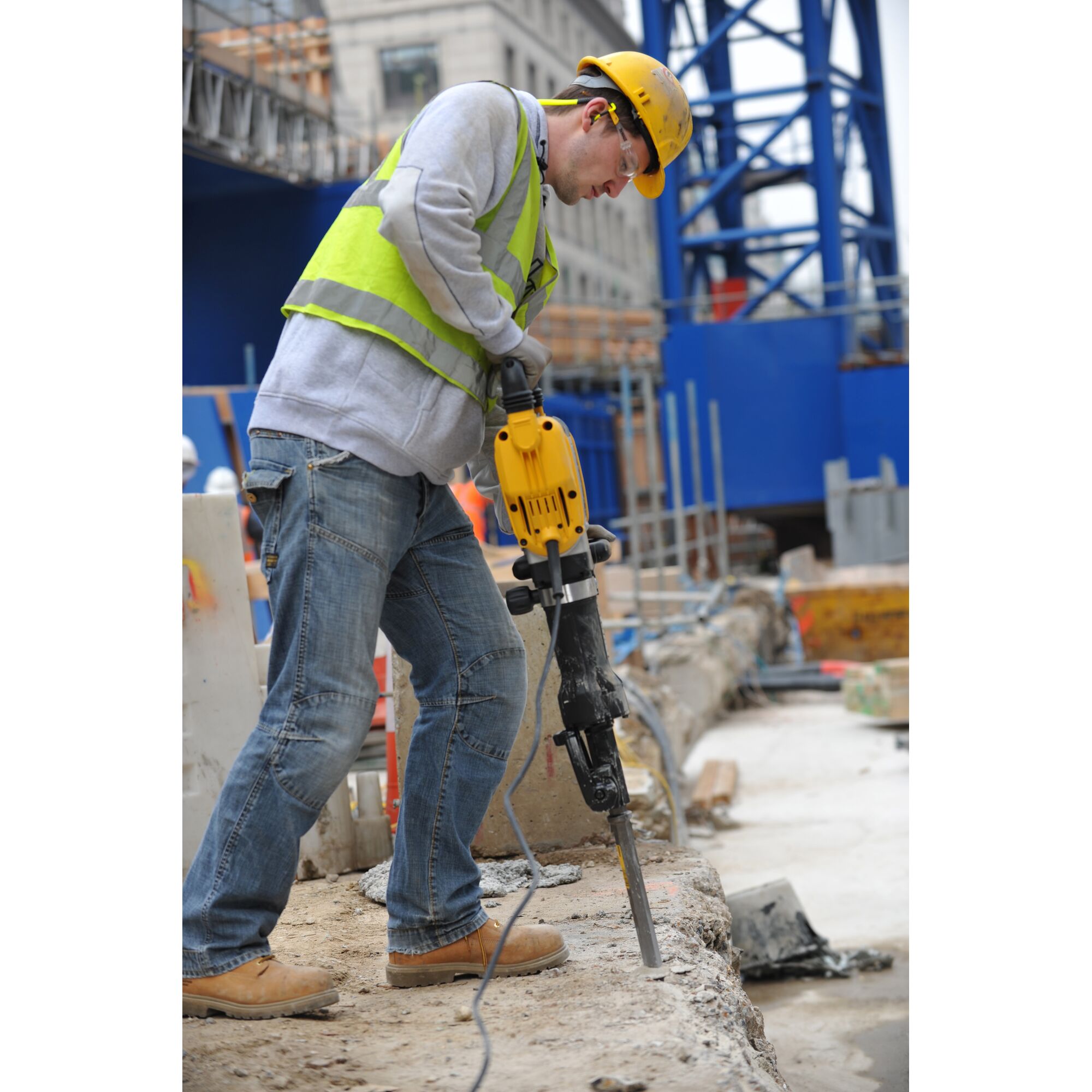 Worker using DEWALT jackhammer DT6927 on concrete at construction site, wearing safety gear and helmet.