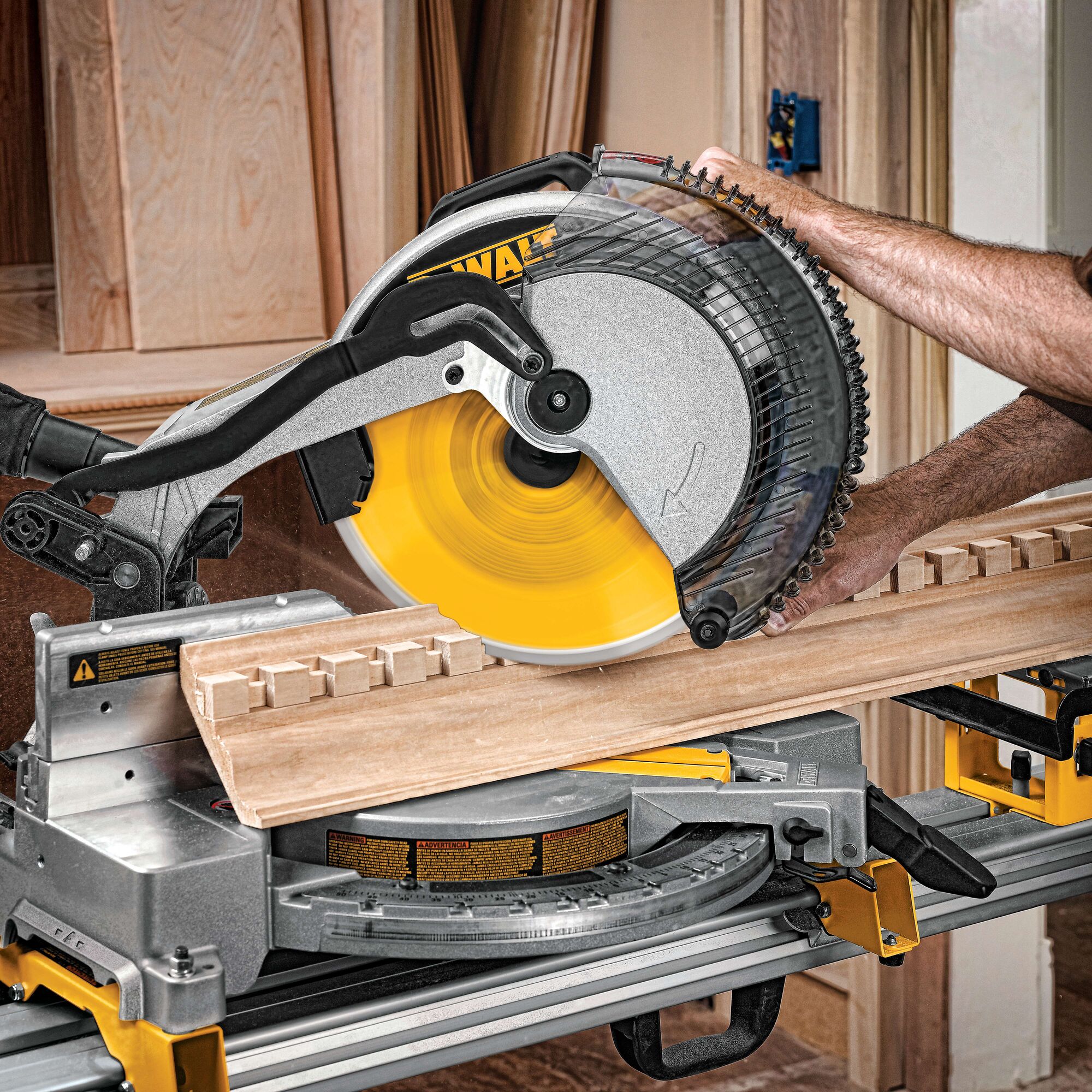 A person is using a DEWALT miter saw with a yellow blade to cut a piece of wood. The saw is mounted on a workbench surrounded by wooden boards.