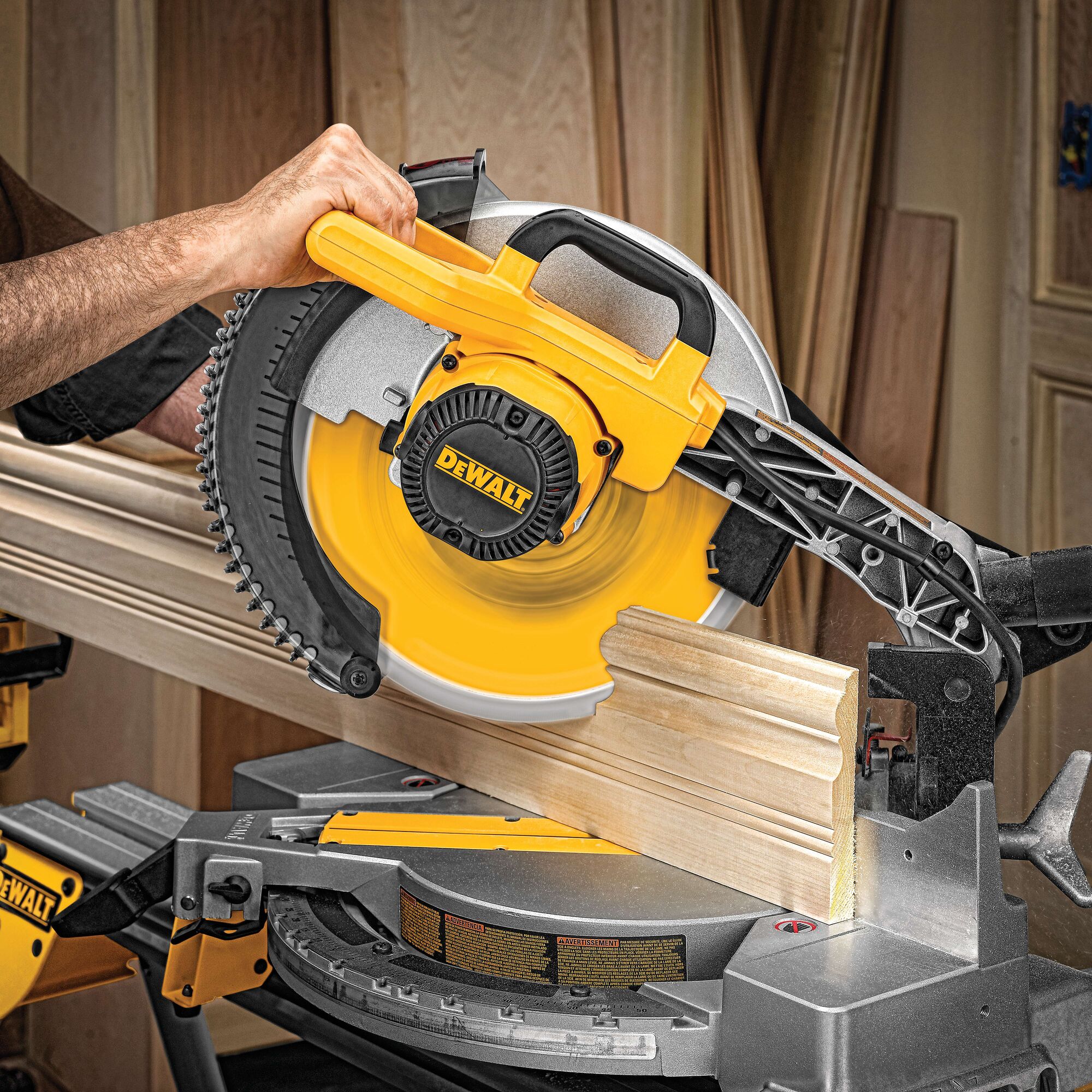 A DEWALT miter saw cutting a piece of wooden molding in a workshop. The saw is being operated by a person and the brand name is clearly visible on the tool.