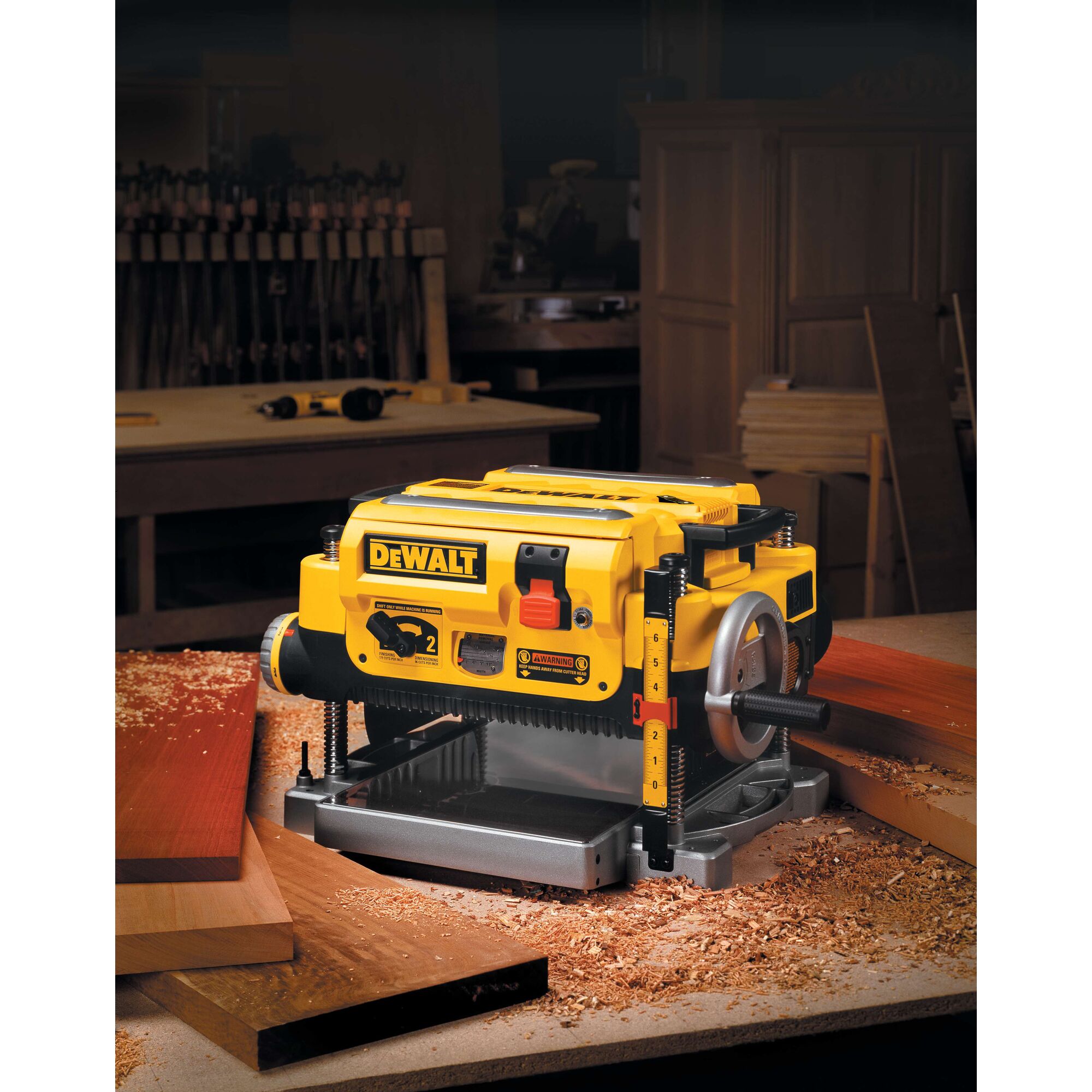 A DEWALT DW735 benchtop thickness planer is shown on a workbench in a woodworking shop, surrounded by wood shavings and wooden boards.