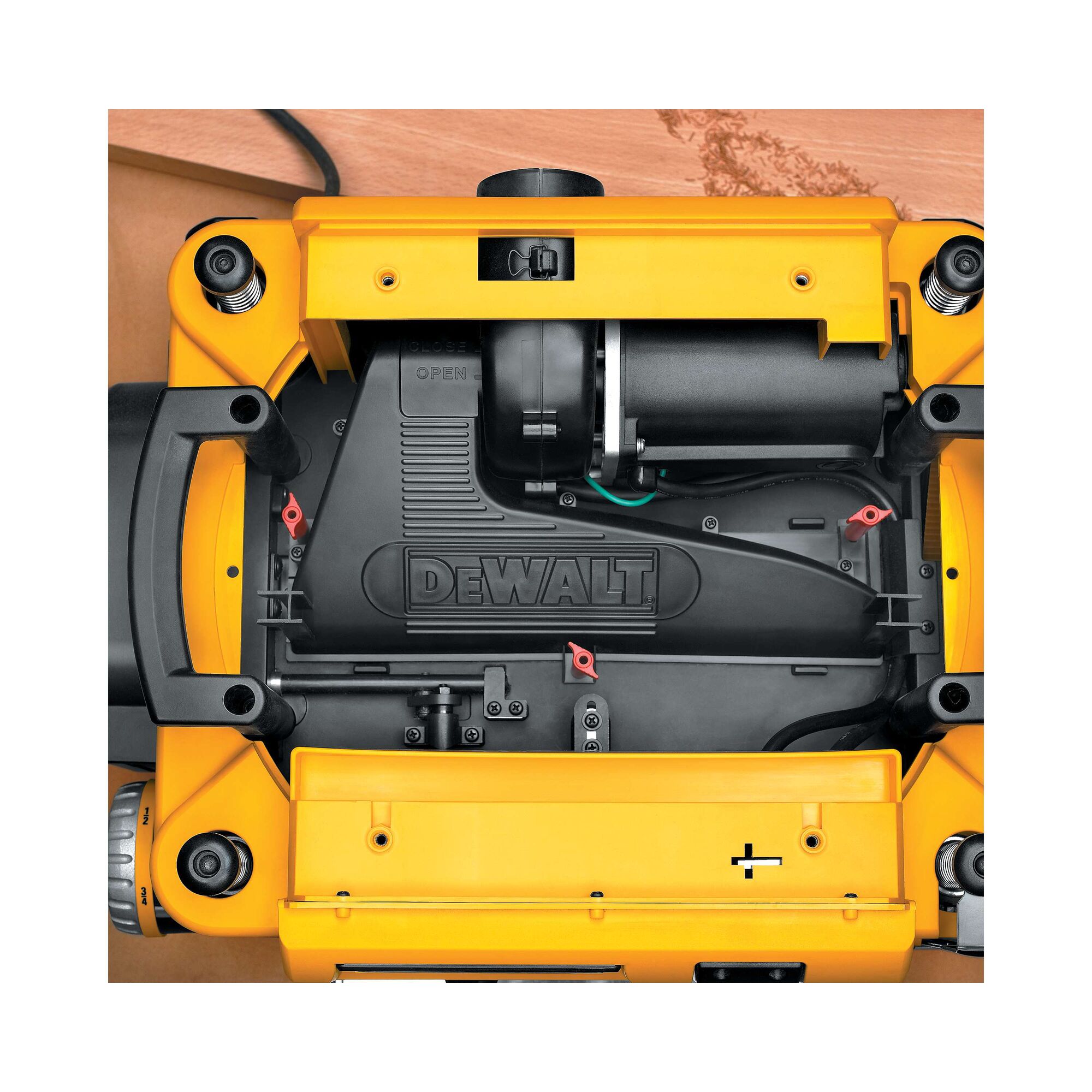 Top view of a DEWALT DW735 wood planer in yellow and black, showing its internal components and mechanical details. The DEWALT logo is visible on the central black cover, and the tool is positioned on a wooden surface.