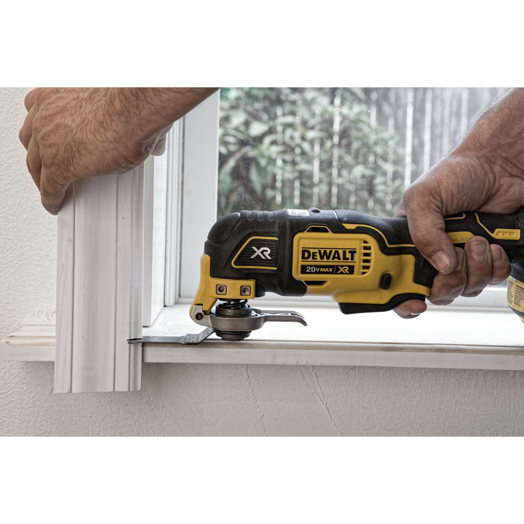 A person uses a DEWALT 20V MAX XR oscillating multi-tool to cut a piece of window trim in a home setting.