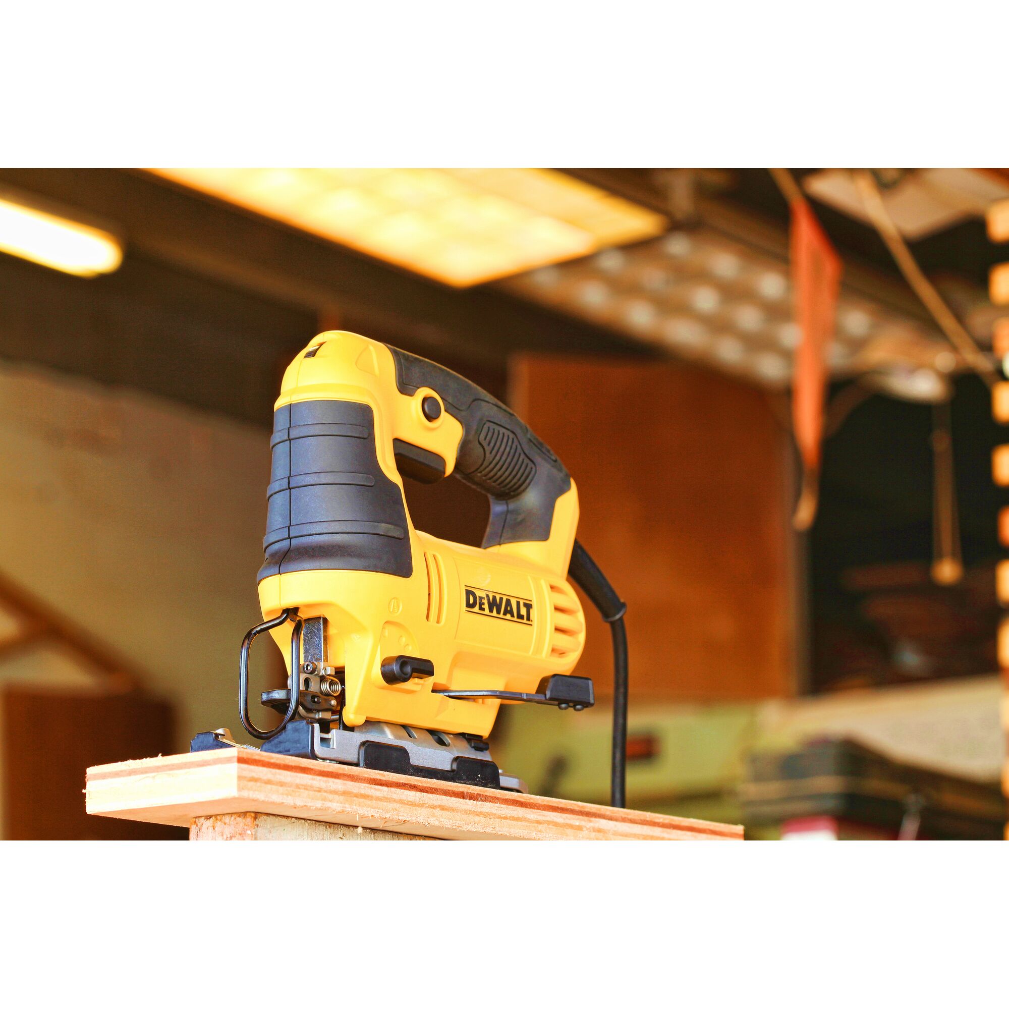 A yellow and black DEWALT jigsaw power tool (model DWE349) positioned on the edge of a wooden board in a workshop setting.