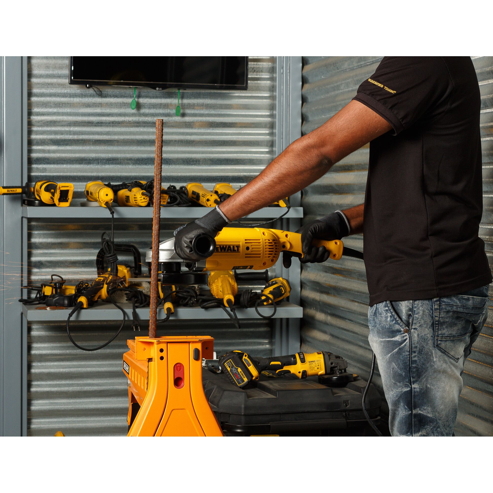 A person using a DEWALT angle grinder to cut a metal rod in a workshop with other DEWALT tools and equipment on shelves in the background.