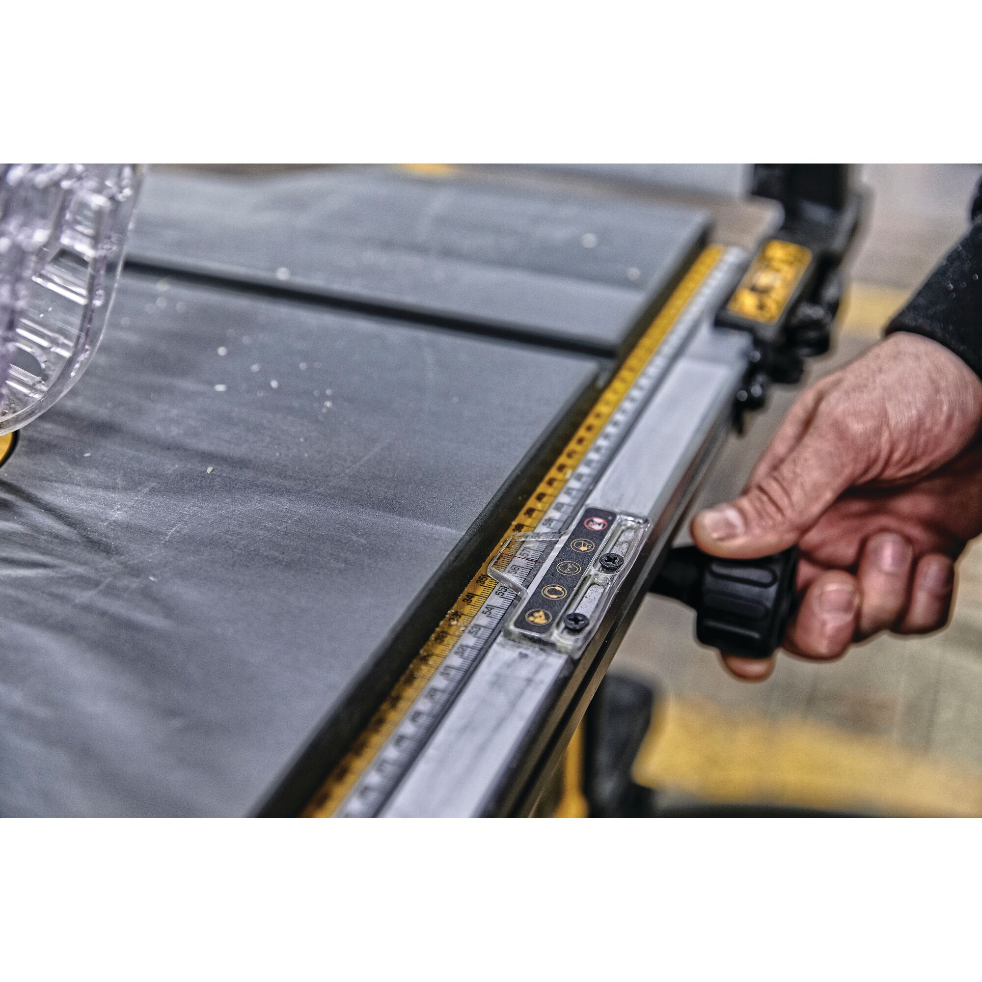 Close-up of a person's hand adjusting the fence of a DEWALT table saw, showing the measuring guide and part of the cutting surface.