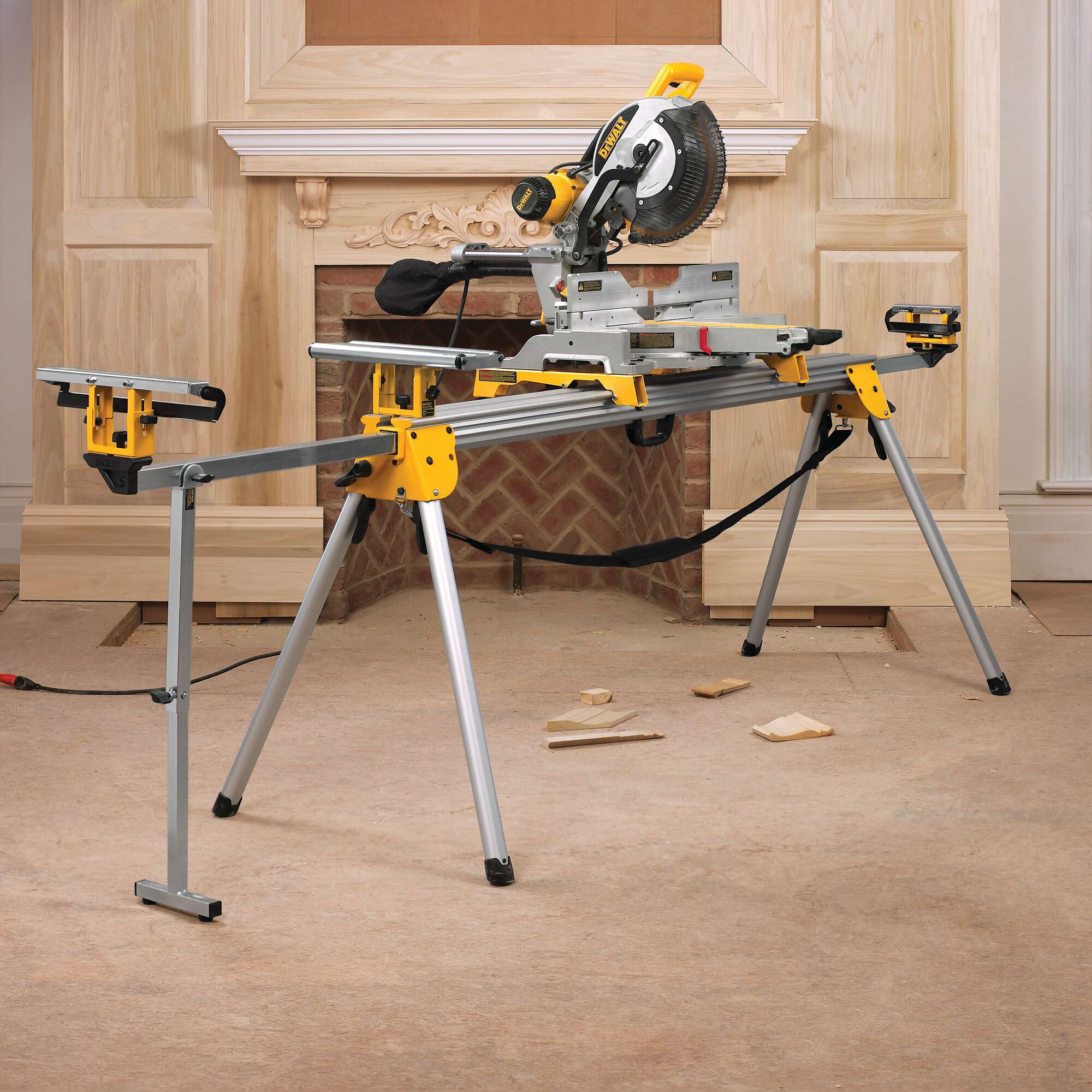 A DEWALT miter saw is set up on a metal stand in a room with unfinished woodwork and tools on the floor. The saw is ready for woodworking tasks.
