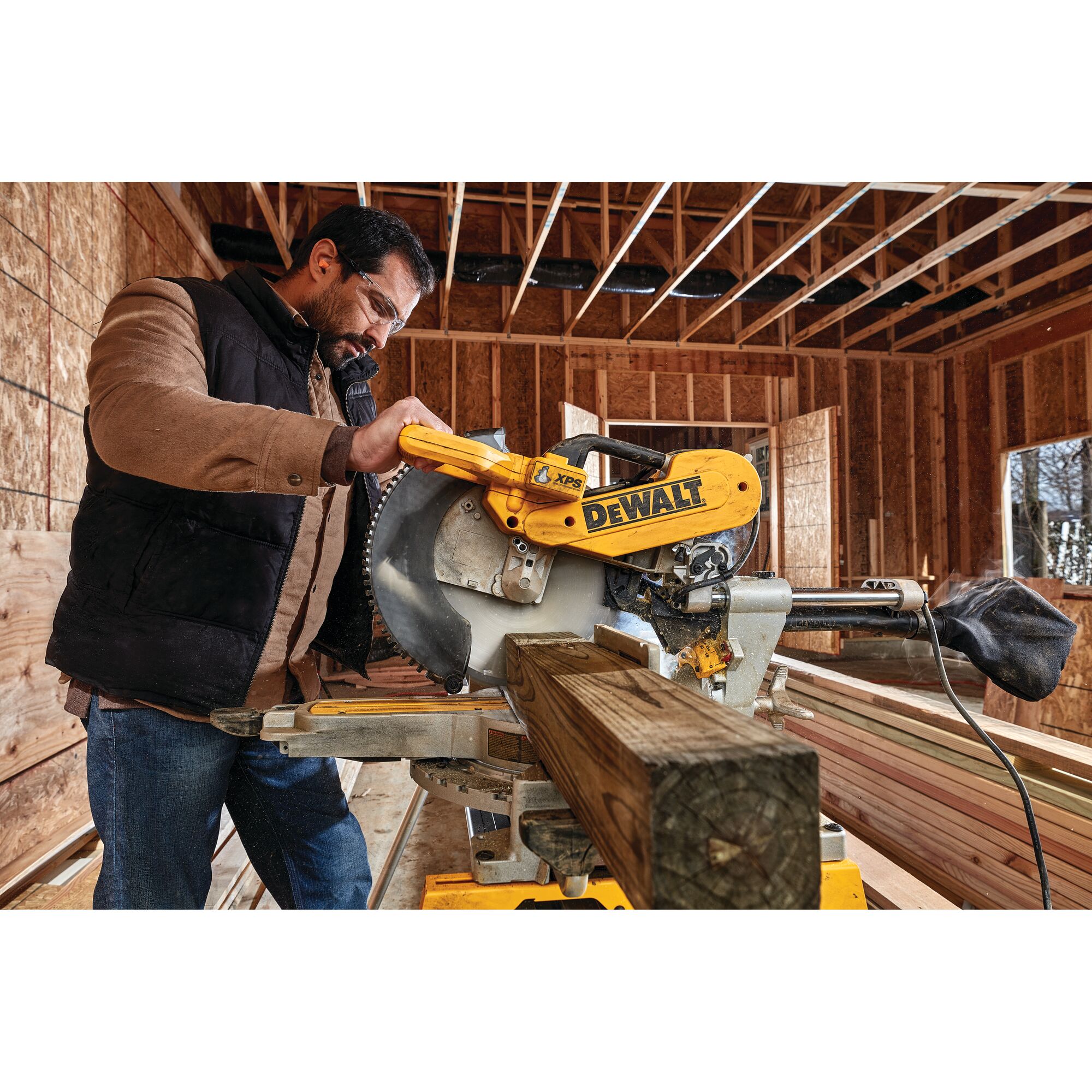 A person operating a DEWALT DWS780 miter saw in a construction site, cutting a wooden beam inside a partially built structure.