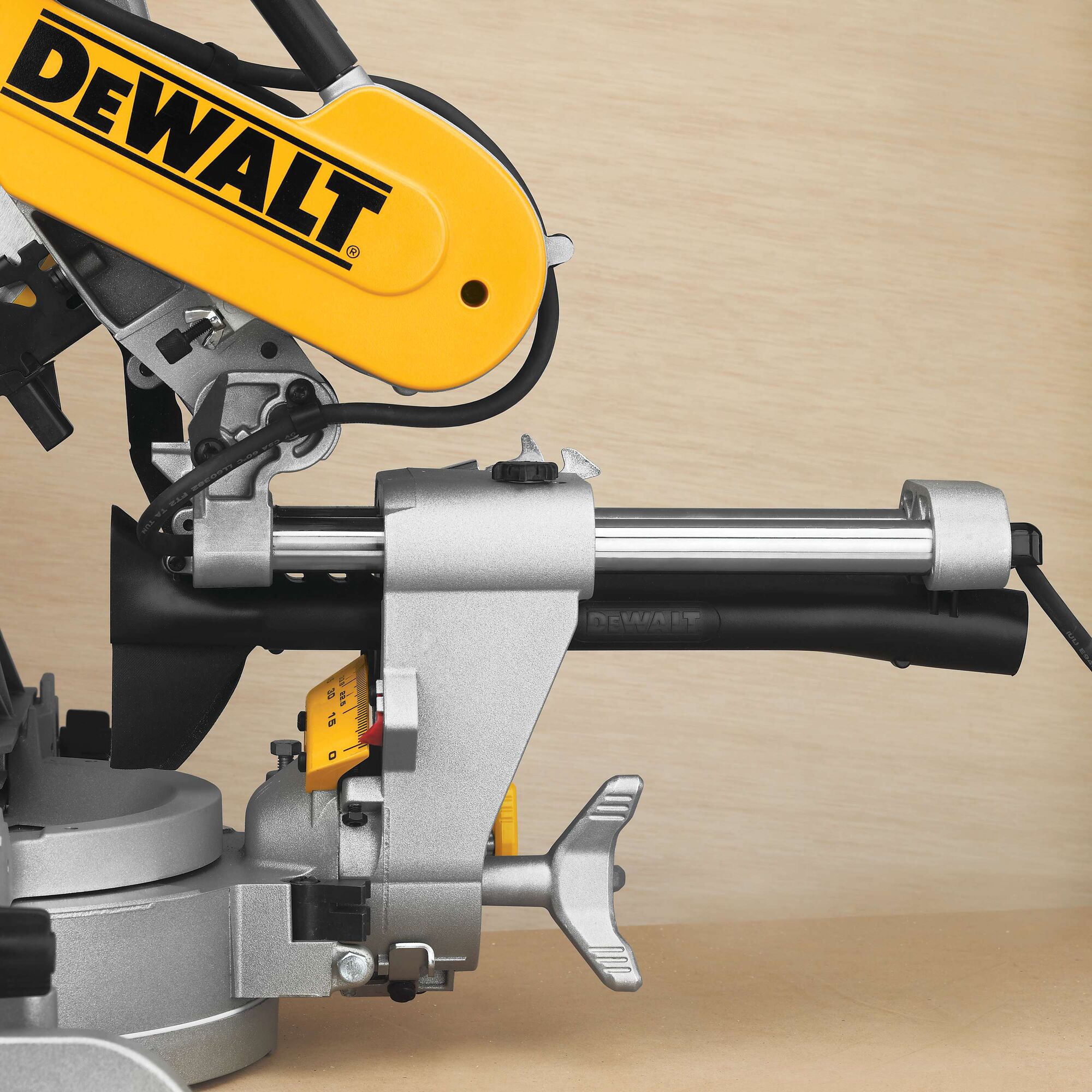 Close-up view of a DEWALT miter saw with a yellow motor housing and metallic components, set against a light wooden background.