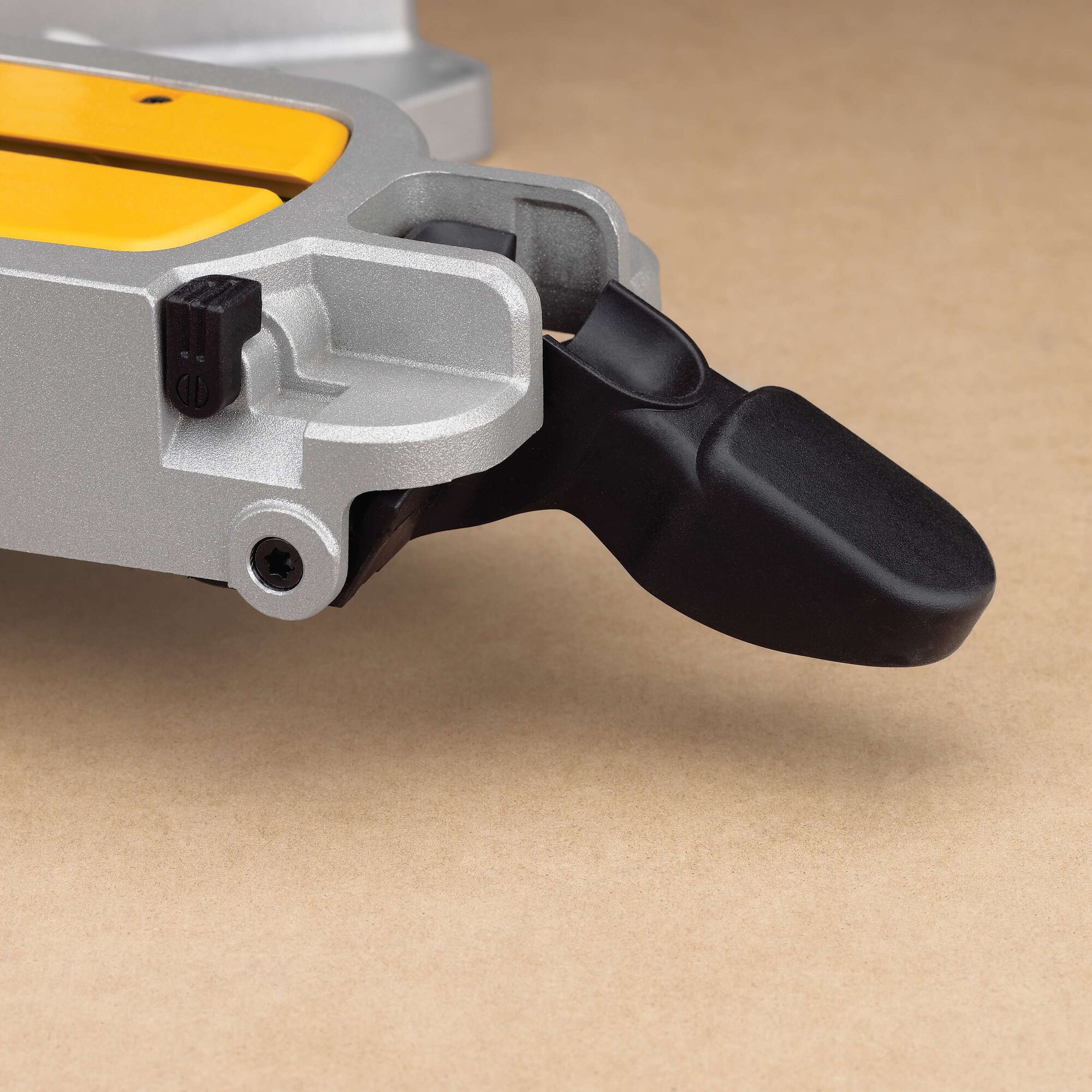 Close-up image of a part of a DEWALT tool, specifically showing a black plastic lever attached to a metallic silver and yellow component, placed on a beige surface.