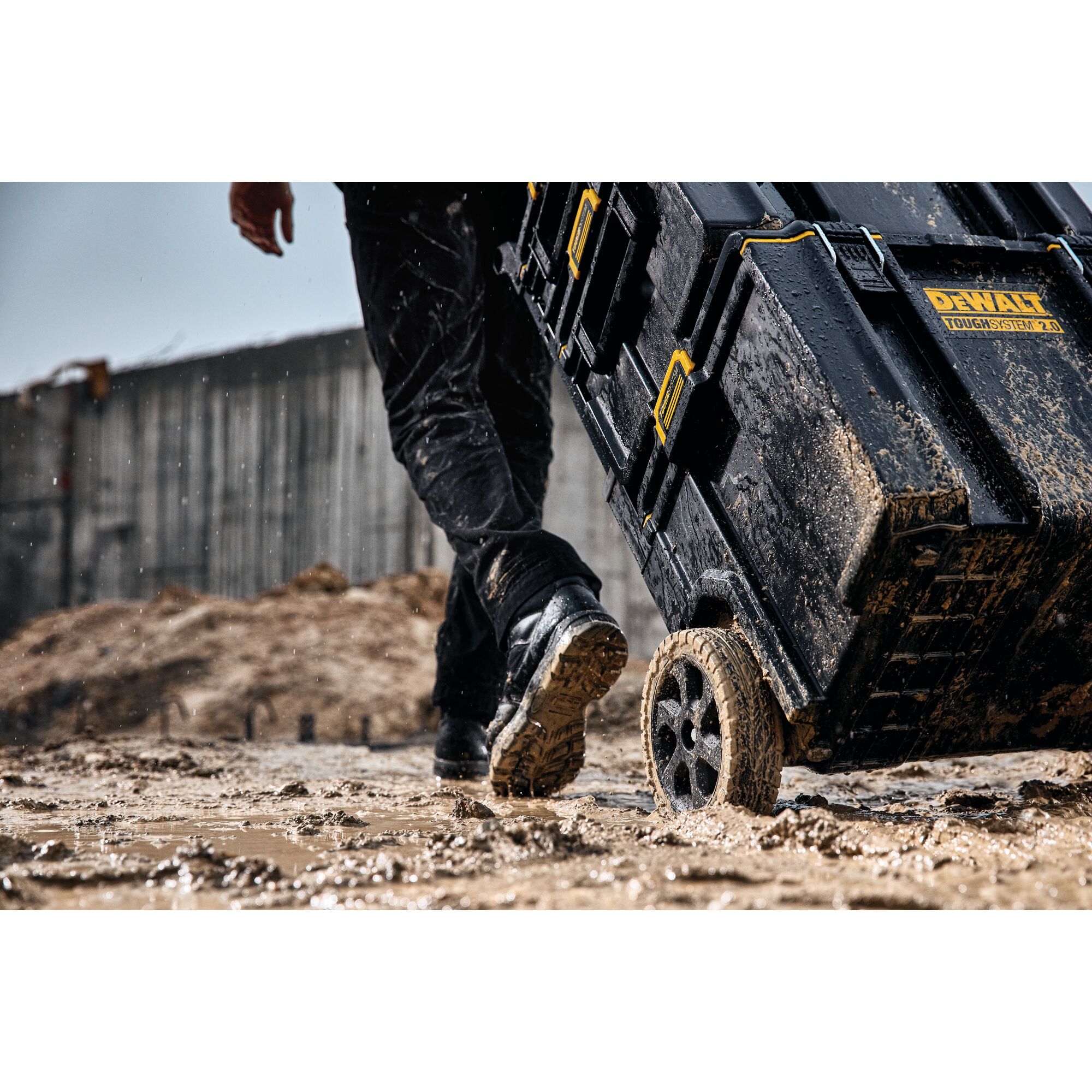 Muddy DEWALT ToughSystem 2.0 toolbox on wheels being pulled across a wet, muddy construction site.