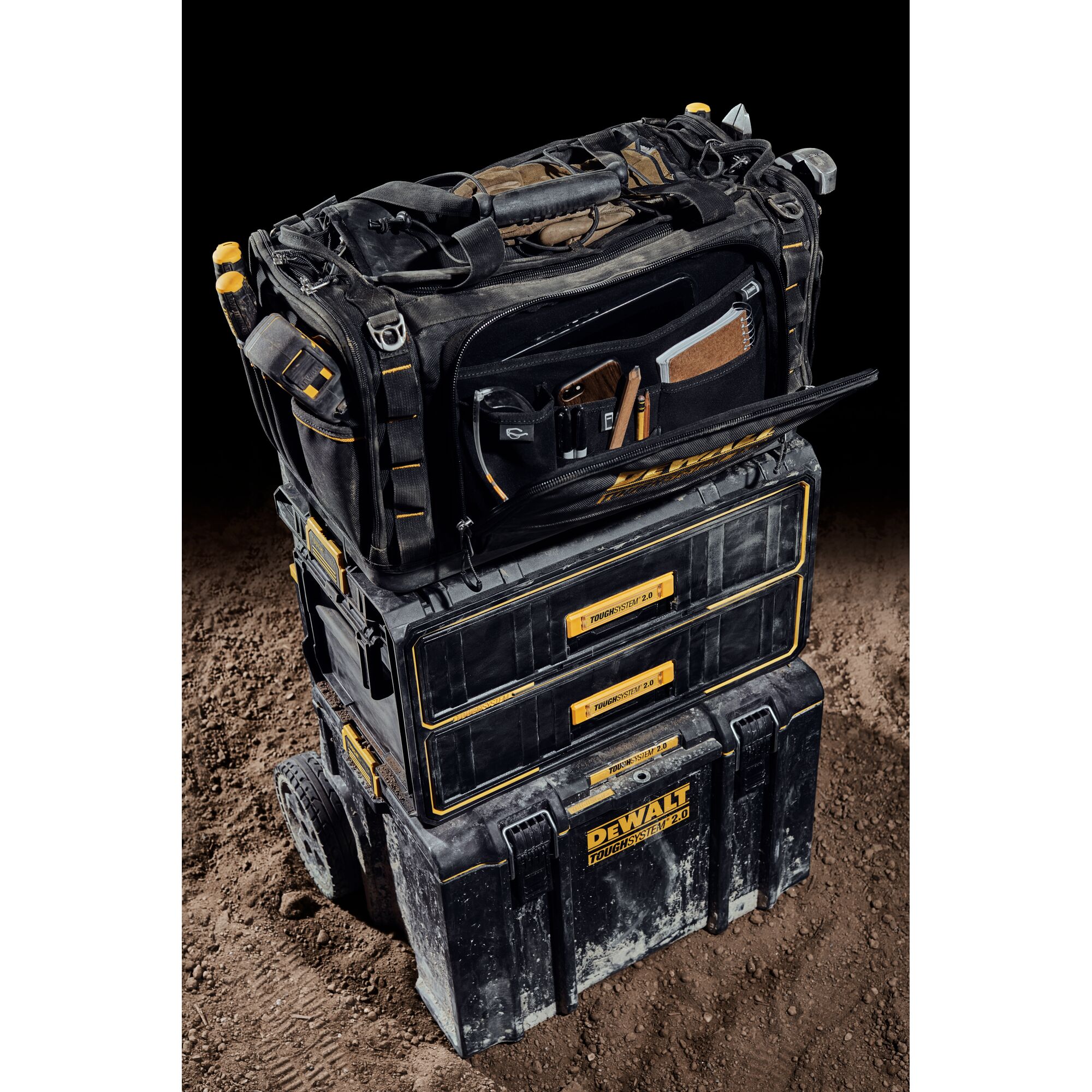 Front view of the DEWALT TOUGHSYSTEM 2.0 22-inch jobsite soft storage toolbag with front pocket open holding various tools on top of TOUGHSYSTEM 2.0 two-drawer organizer.